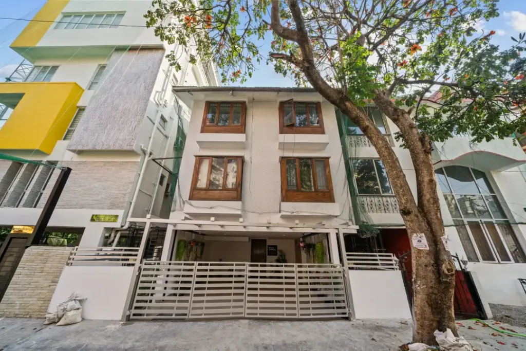 The striking contemporary exterior of Namma Woodland in Domlur, seamlessly integrated with towering trees and a lush, forest-like landscape.