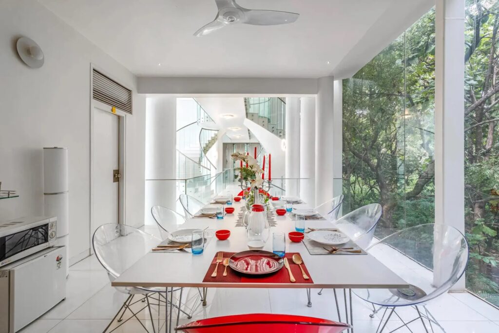 Modern open-concept dining area at Crystal Hall by Spacez, showing a large contemporary table setup for a group party, surrounded by all-glass architecture and scenic outdoor nature views.