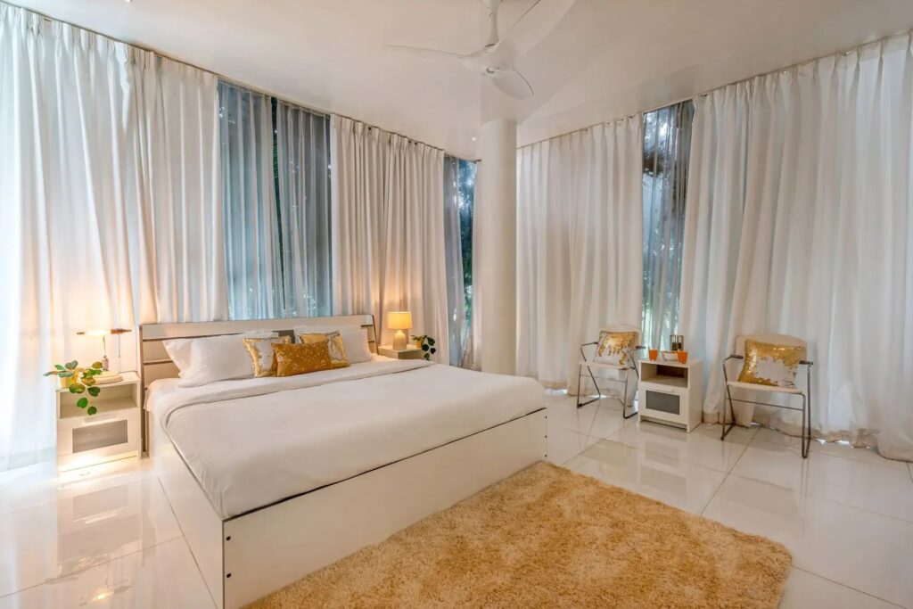 Serene luxury bedroom at Crystal Hall with a minimalist design, premium white bedding, and floor-to-ceiling glass walls offering a peaceful, immersive view of the surrounding nature and forest.