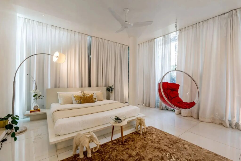 Interior of a luxury bedroom at Crystal Hall featuring floor-to-ceiling glass walls, premium wooden flooring, and a minimalist plush bed with a panoramic view of the surrounding greenery.