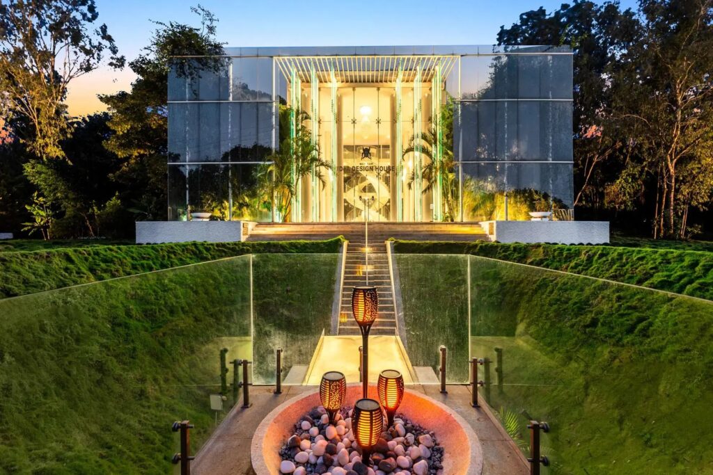 Exterior front view of Crystal Hall, a luxury two-story all-glass villa in Rampura Bengaluru, featuring modern architectural design and a lush green lawn.