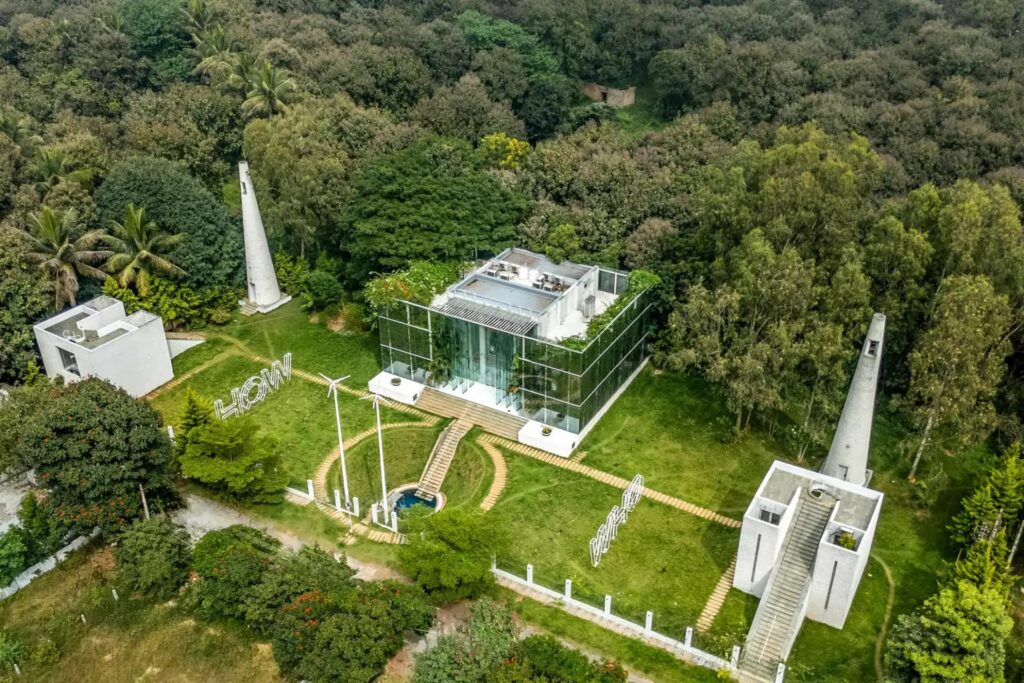 Aerial drone shot of Crystal Hall in Rampura, showcasing the unique all-glass architectural layout, rooftop garden, and surrounding green landscapes in Bengaluru East.