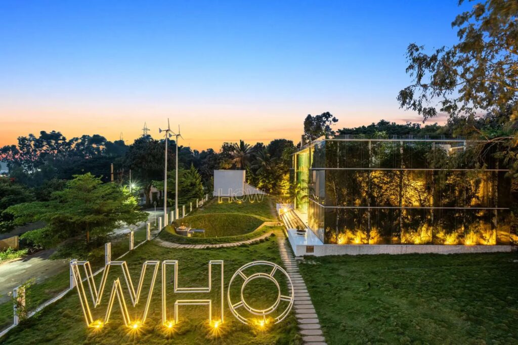 Lush private garden at Crystal Hall Bengaluru with manicured lawns, tropical plants, and a serene fire bowl area, highlighting the eco-friendly "Five Elements" design.