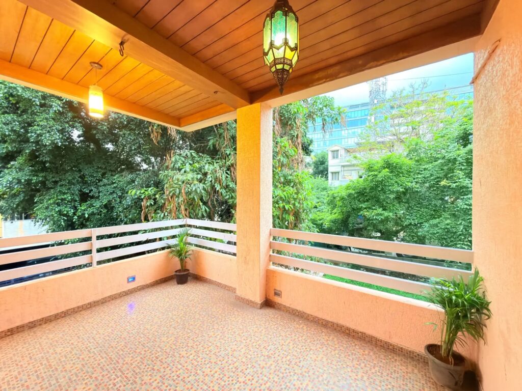 Wide glass-front balcony lounge attached to a luxury villa bedroom overlooking a green residential neighborhood.
